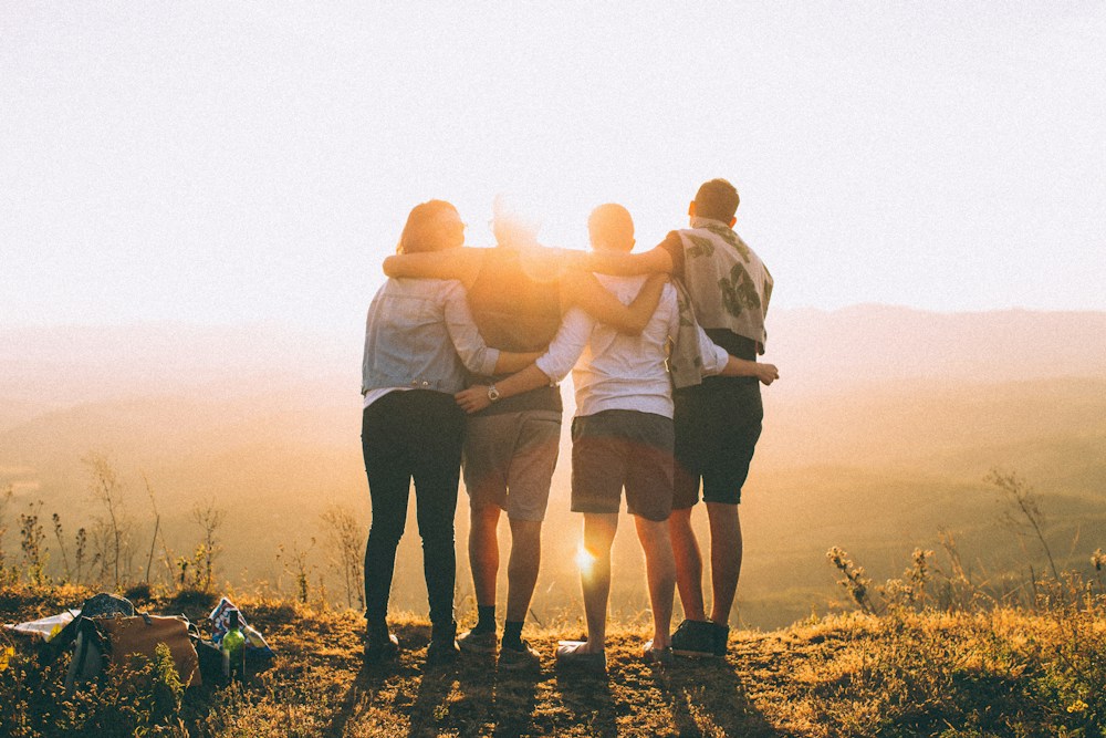 Four people standing together with their arms around one another outdoors